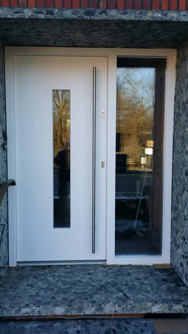 Białe drzwi wejściowe z&nbsp;pionowym przeszkleniem i&nbsp;bocznym doświetlem